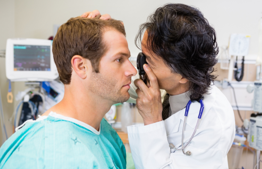 General practitioner examines a patient’s eye with a handheld ophthalmoscope in a clinical room, illustrating reliance on traditional single-purpose tools.